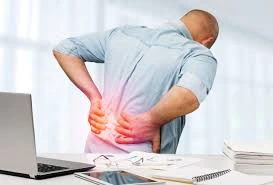Office professional standing at a desk suffering from severe lower back pain and sciatica, highlighting the need for expert spine treatment.